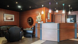 Zona de recepción con mostrador de madera, espejo redondo, sofá de cuero negro y planta en maceta.