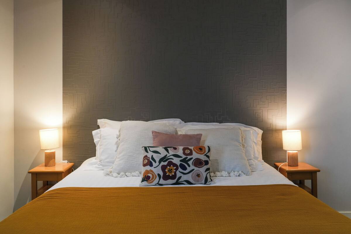 A neatly made bed with a floral pillow, two bedside lamps, and a wooden headboard.