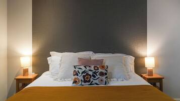 Una cama bien hecha con un cojín floral, dos lámparas de noche y un cabecero de madera.