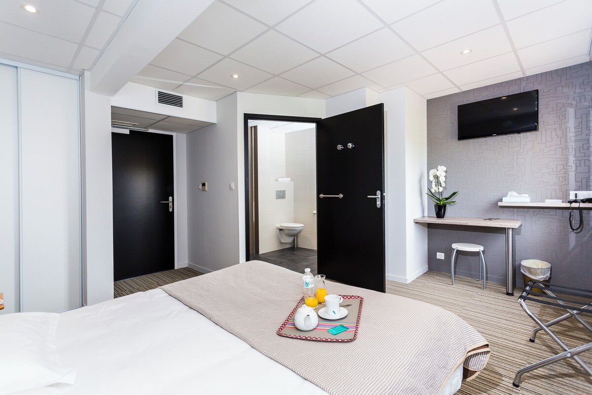 Een hotelkamer met een bed, een ontbijttafel, een bureau, een televisie en een badkamer.