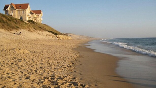 Una playa arenosa con una casa sobre una duna.