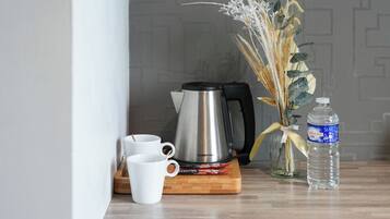 Une cafetière en acier inoxydable, des tasses blanches, une planche à découper en bois, une bouteille d’eau et un vase contenant des plantes séchées, le tout posé sur une surface en bois.