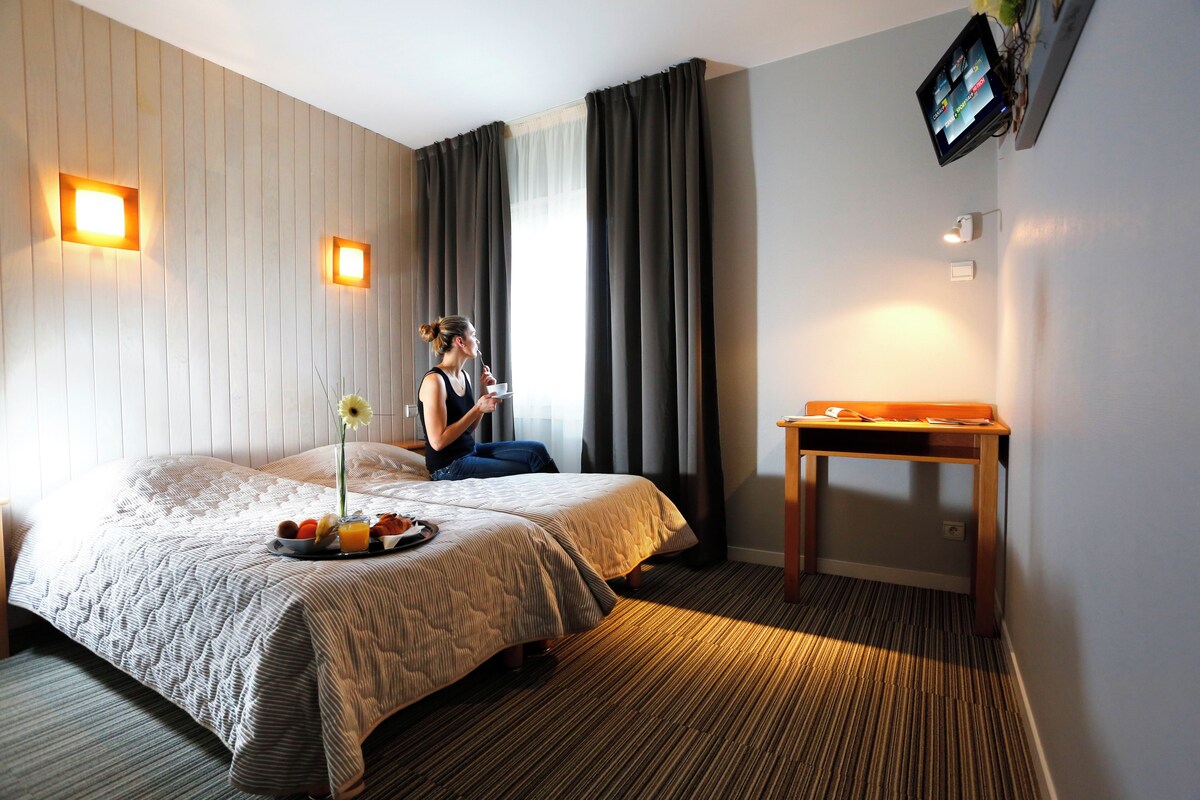 Hotelkamer met een bed, nachtkastje, tv aan de muur en een raam met gordijnen.