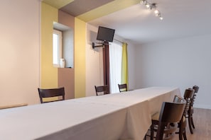 Une salle de conférence avec une longue table, des chaises, un téléviseur à écran plat et une fenêtre avec des rideaux.