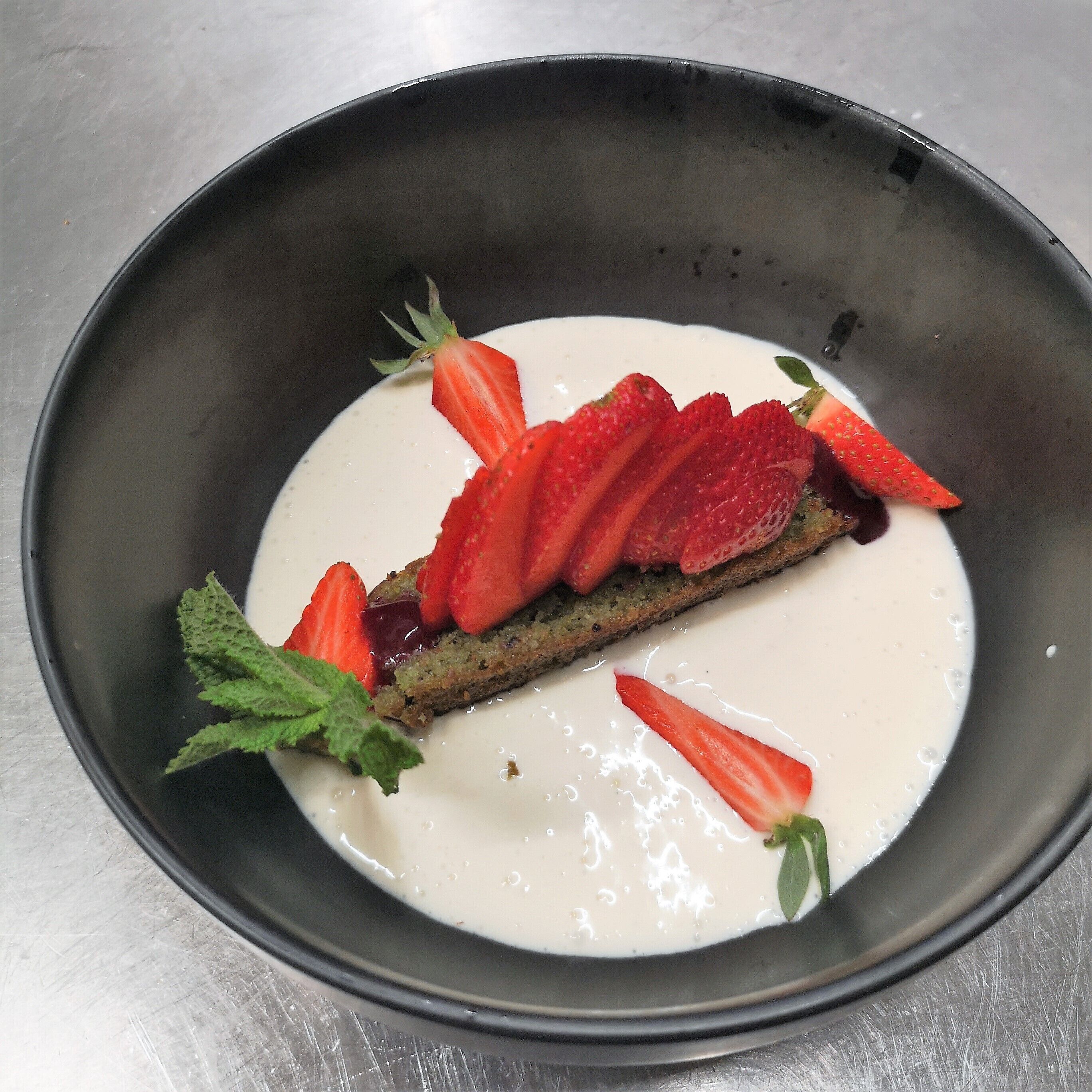 A dessert with strawberries and a mint leaf on a plate.