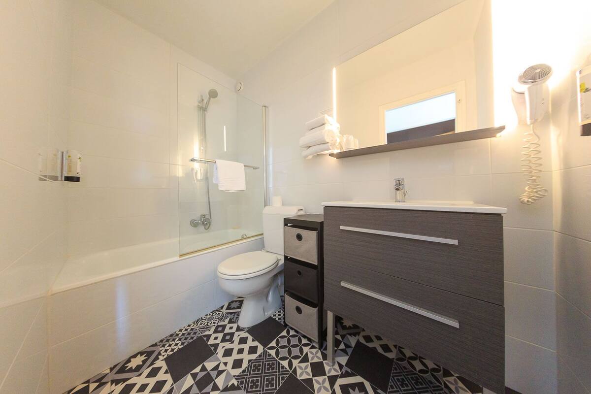 Een moderne badkamer met een douchecabine van glas, een toilet, een wastafel met spiegel en vloertegels met een patroon.