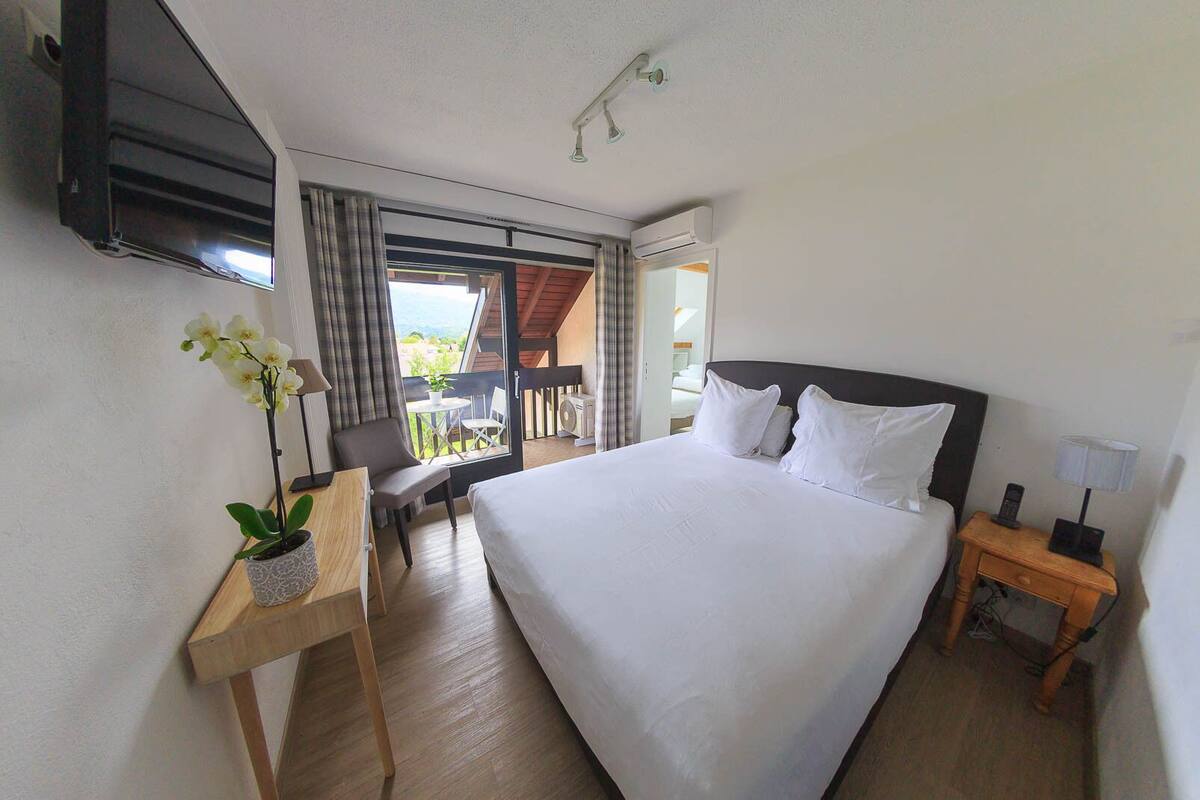 Hotelkamer met een groot bed, een bureau met een plant, een stoel, een klein tafeltje en een balkon met een tafel en stoelen.
