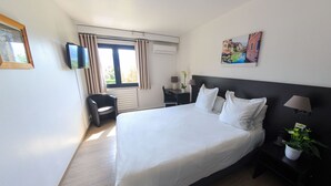 A hotel room with a large bed, a desk, a chair, a TV, and a window with curtains. - Logis Hôtel Annecy Nord / Argonay (Argonay)