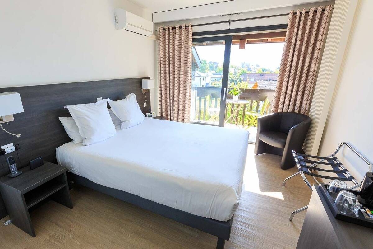 Een hotelkamer met een groot bed, een bureau met koffiezetapparaat, een stoel en een balkon met gordijnen.