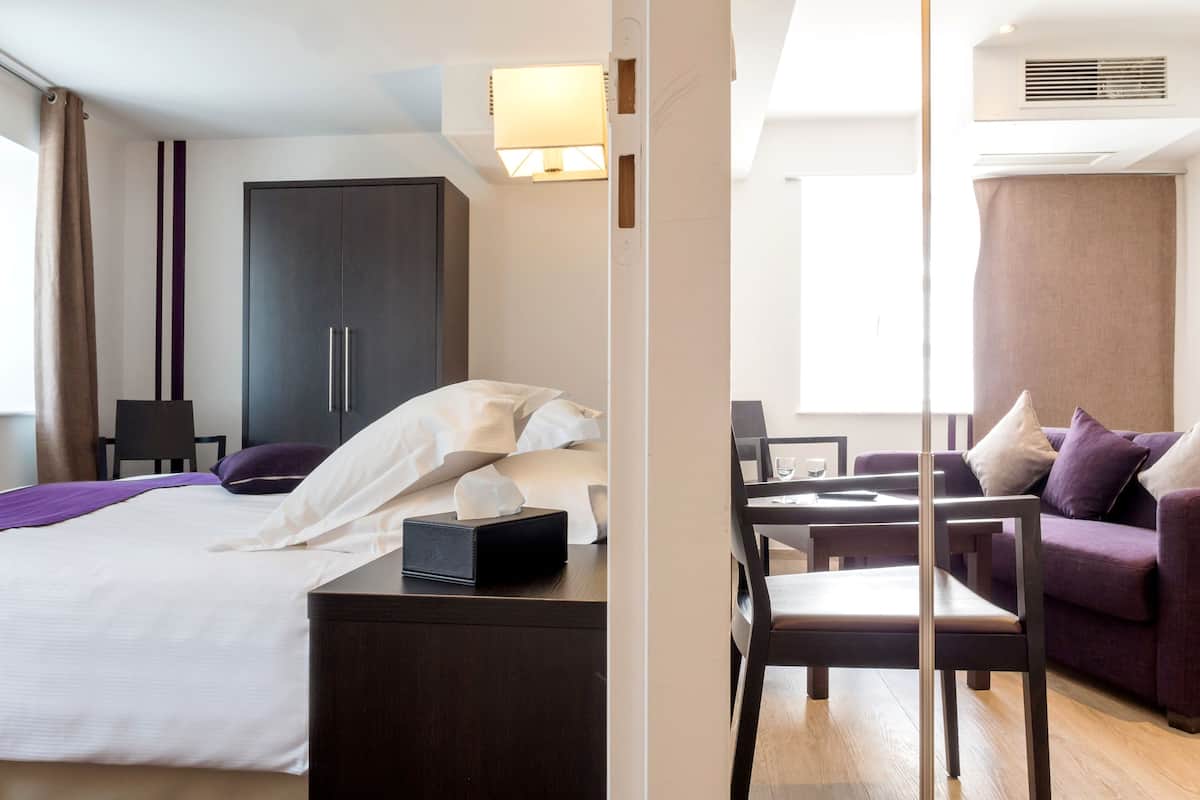 A hotel room with a bed, a desk, a chair, a wardrobe, and a sofa.