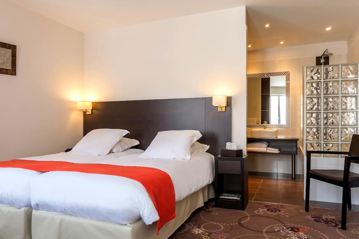 A hotel room with a bed, bedside lamps, a desk, a chair, and a bathroom with a mirror and sink.