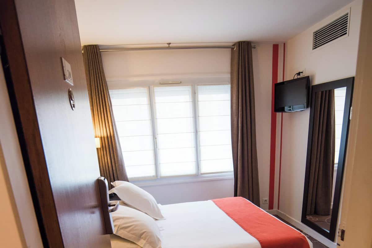 A hotel room with a bed, a television mounted on the wall, and a window with curtains.