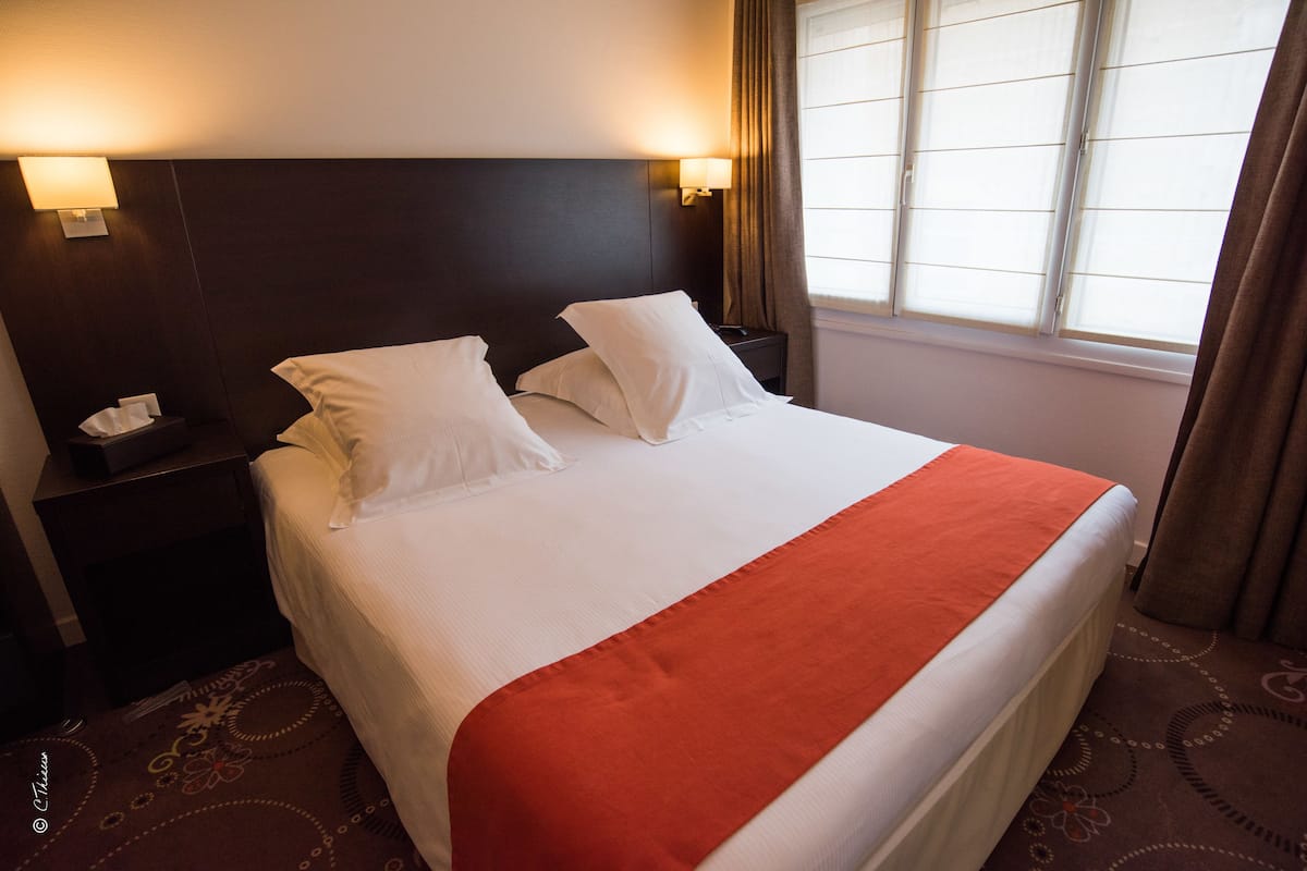 A hotel room with a large bed, two bedside lamps, a nightstand, and a window with curtains.