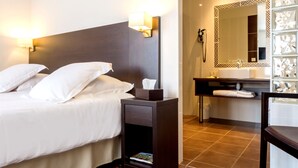 A hotel room with a bed, bedside lamps, a nightstand with a book, a bathroom with a mirror, sink, and towel rack. - Chez La Rose (Juliénas)