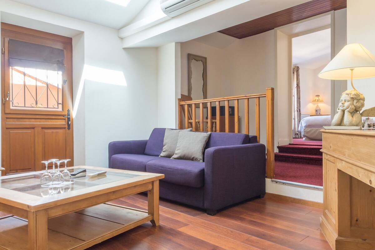 A living room with a purple sofa, wooden coffee table, and a staircase leading to a bedroom.