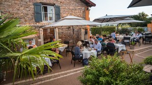An outdoor dining area with stone walls, tables, and umbrellas. - Chez La Rose (Juliénas)