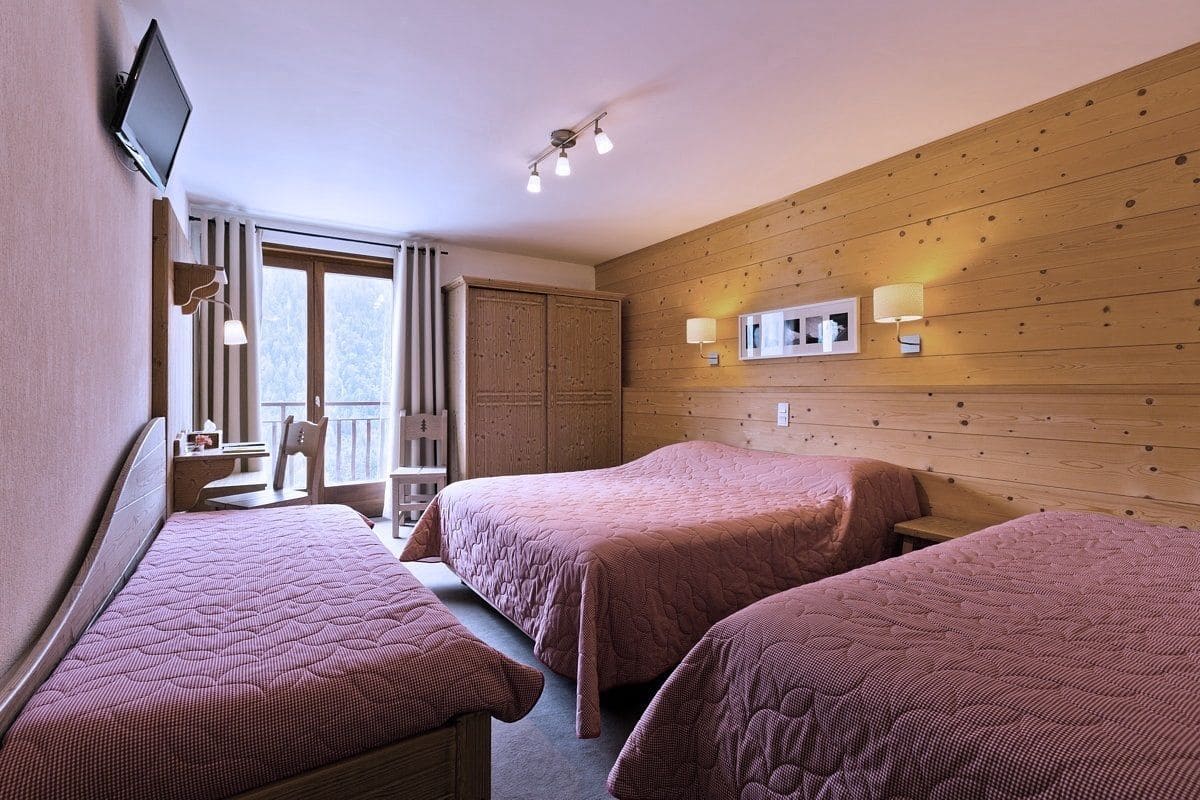 A hotel room with two beds, a desk, a chair, and a TV.