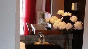 Un baño con lavamanos, espejo y un florero de flores blancas.