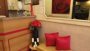 Zona de recepción con mostrador, un jarrón de flores rojas, una mesita con velas y cojines rojos.