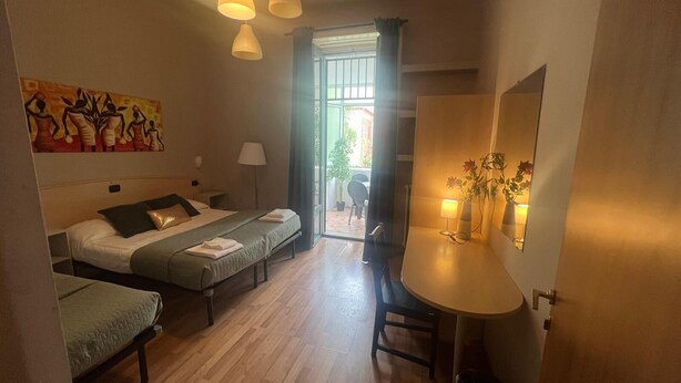 Una habitación de hotel con una cama, dos mesitas de noche, un escritorio, una silla y una ventana con cortinas.