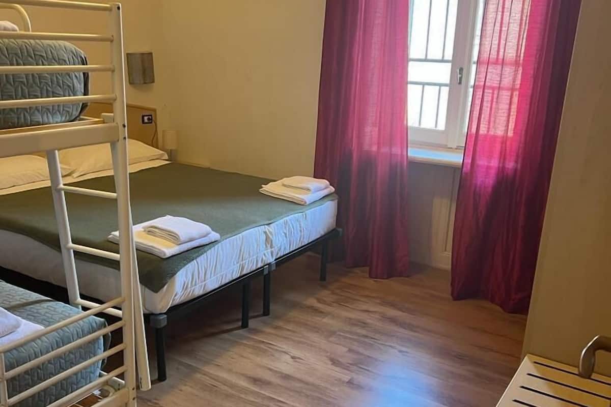 Ein Schlafsaalzimmer mit Etagenbetten, einem Fenster mit roten Vorhängen und einem Holzboden.