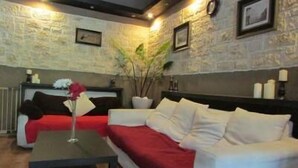 Una habitación acogedora con un sofá blanco, una manta roja y una mesa de centro negra. Hay una planta a un lado y un cuadro en la pared.