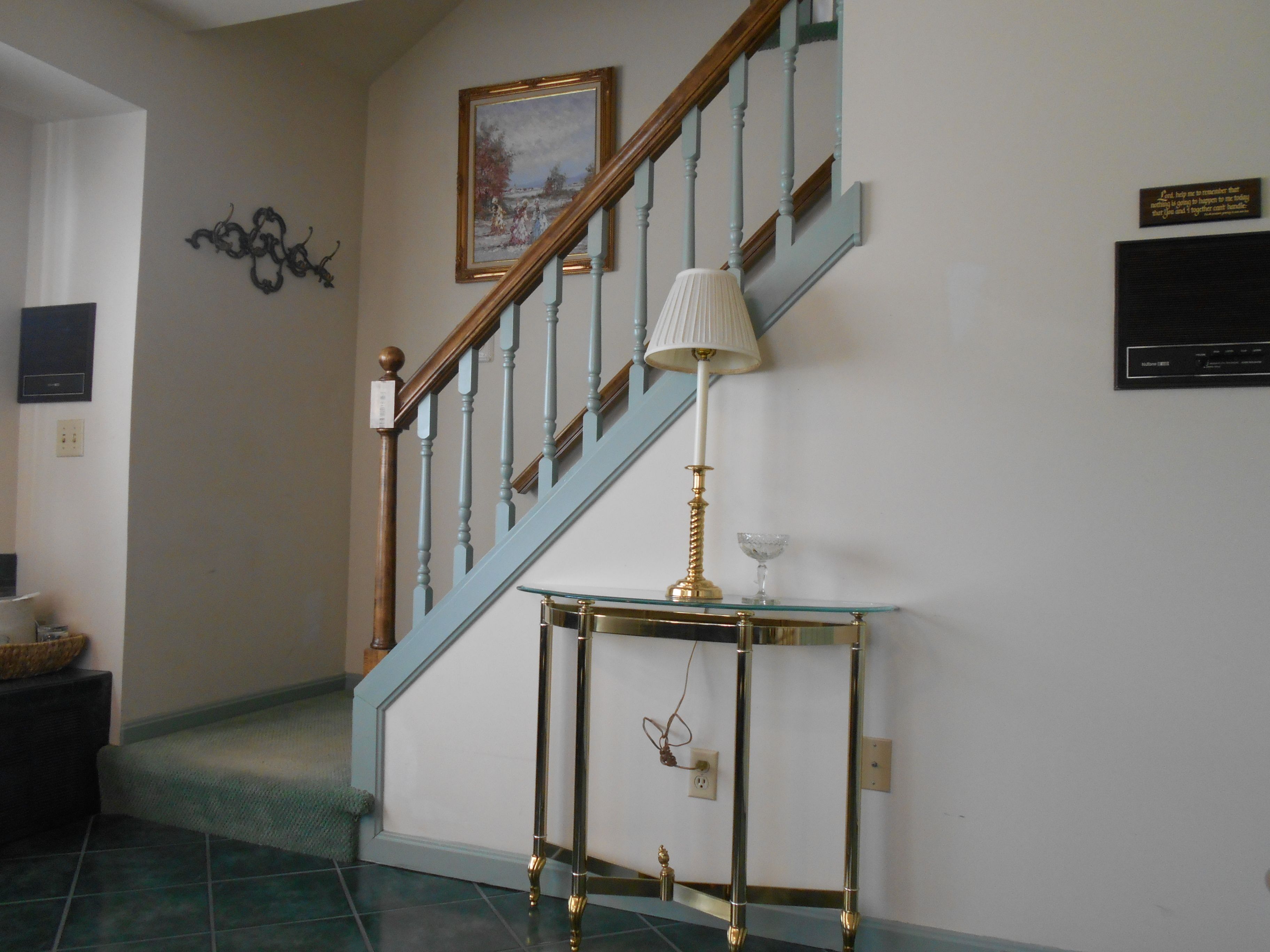 A staircase with blue railings, a glass-top console table with a lamp, and a framed picture on the wall.