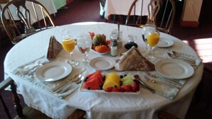 A round dining table with a white tablecloth, set with plates, cutlery, and a fruit platter. - West Ridge Bed and Breakfast (Elizabethtown)