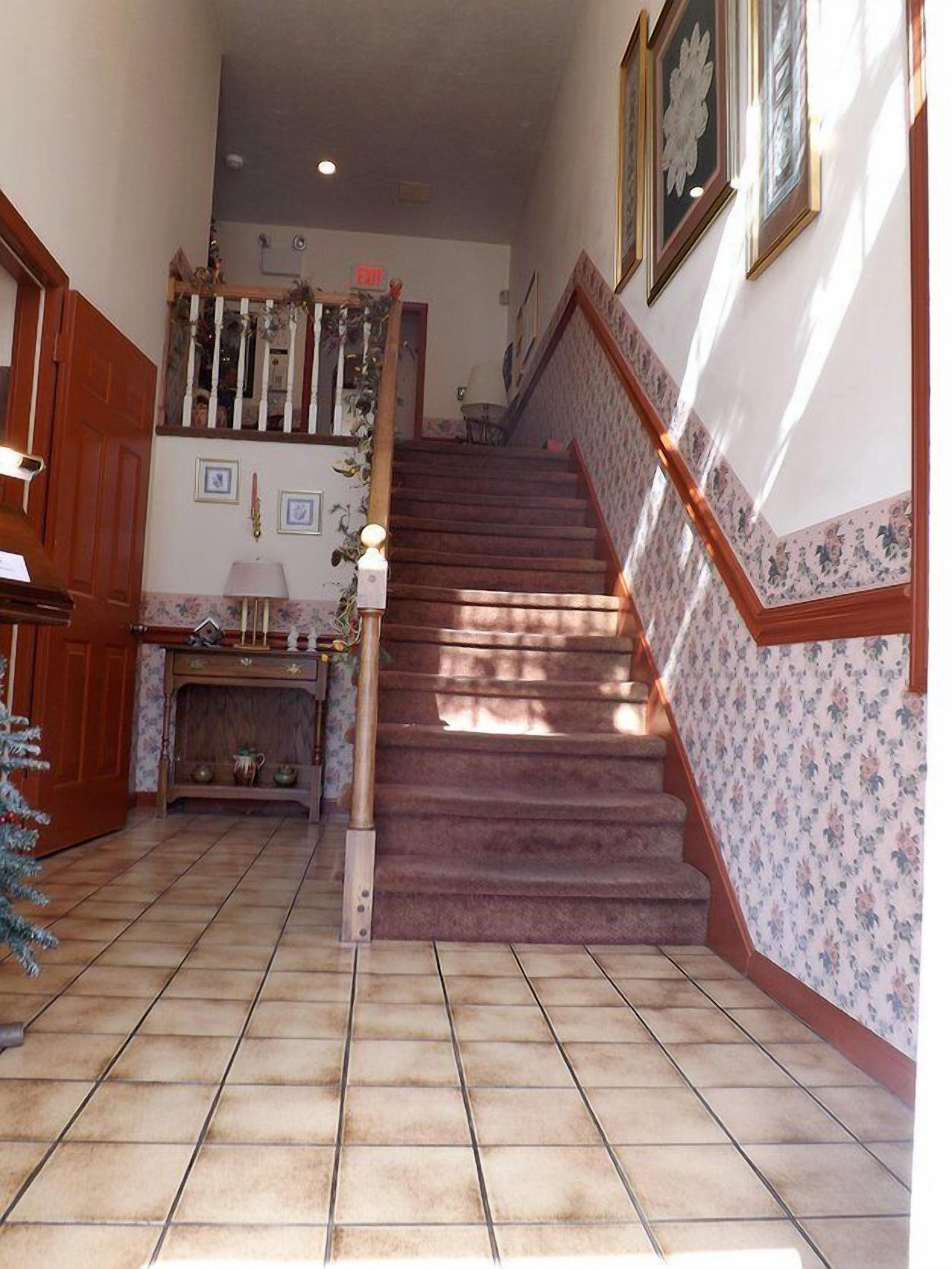 A staircase with a wooden handrail and a tiled floor leading to a landing.