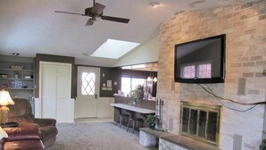 A living room with a fireplace, a TV mounted on the wall, a ceiling fan, and a seating area with a couch and chairs. - West Ridge Bed and Breakfast (Elizabethtown)