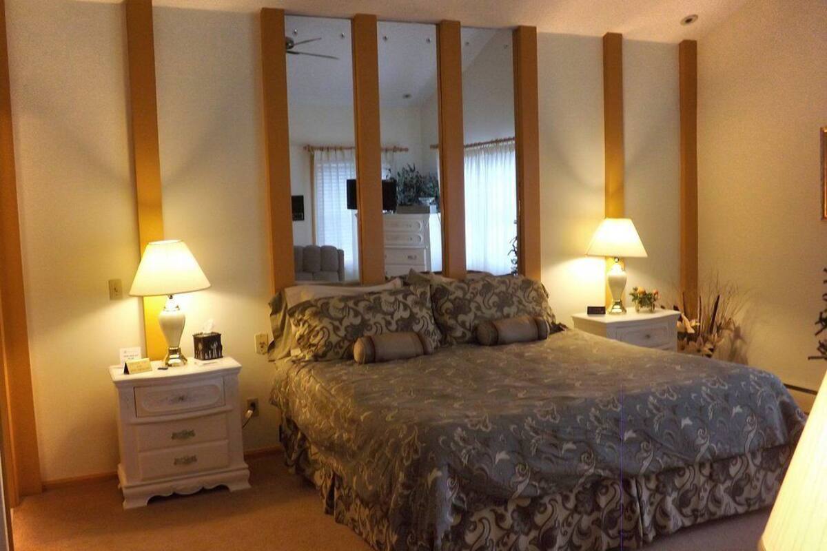 A bedroom with a large bed, two bedside tables, a mirror, and two lamps.