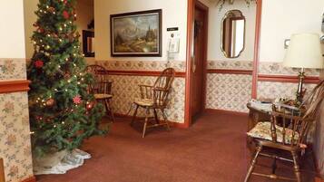 A hotel lobby with a Christmas tree, wooden chairs, a painting on the wall, and a mirror.
