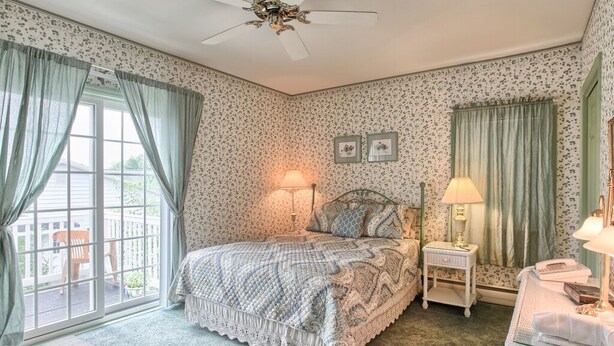 A bedroom with a bed, two bedside tables with lamps, a ceiling fan, and a view through a window. - West Ridge Bed and Breakfast (Elizabethtown)
