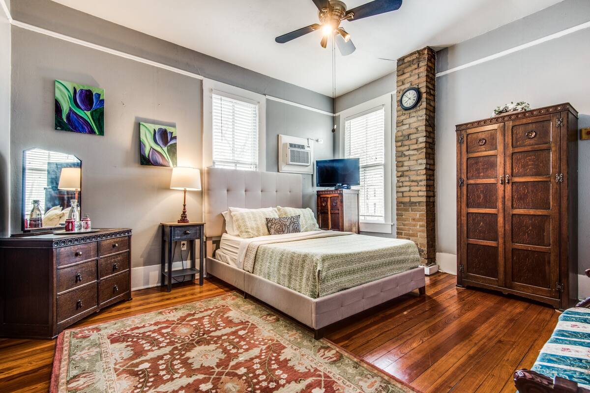 A bedroom with a bed, dresser, TV, and a clock on the wall.