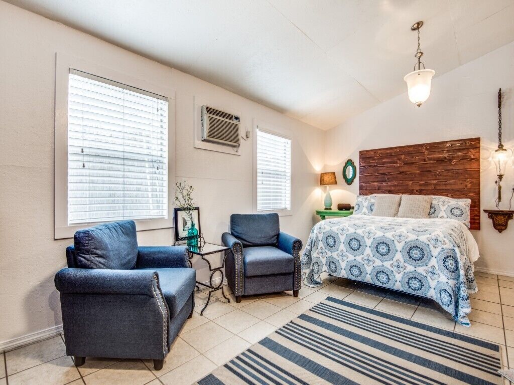 A bedroom with a bed, two armchairs, a small table, and a window with blinds.