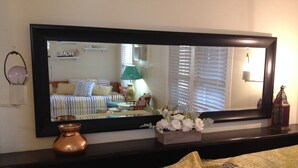 A bedroom with a large mirror, a bed with patterned bedding, a bedside table with a vase, and a decorative lantern. - O'Casey's Boutique Inn (San Antonio)