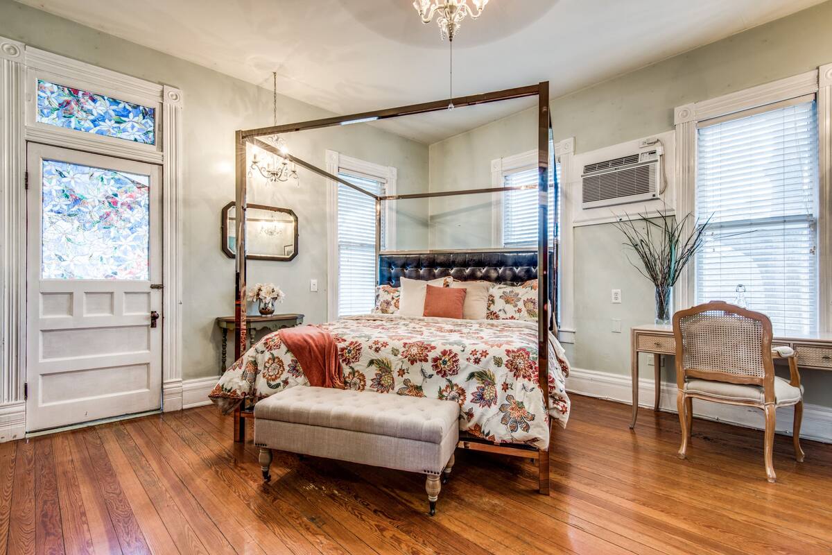 A four-poster bed with a floral bedspread, a wooden bench, and a desk with a chair.