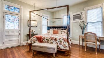 A four-poster bed with a floral bedspread, a wooden bench, and a desk with a chair.