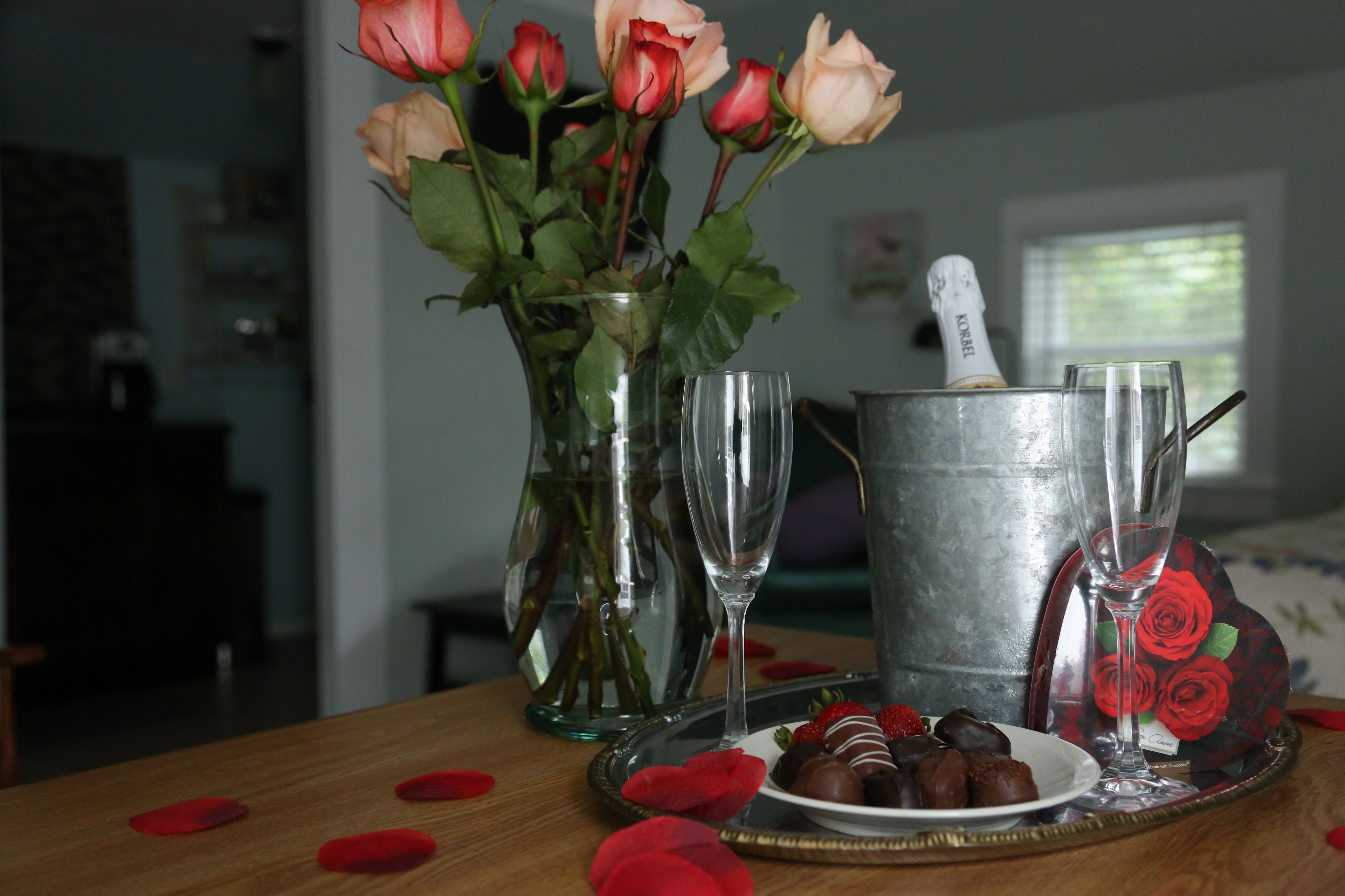 A table with a vase of roses, a champagne bottle, and a plate of chocolates.