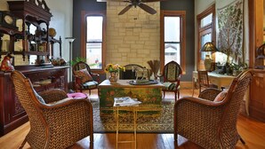A spacious living room with a fireplace, a ceiling fan, and a variety of furniture including wicker chairs and a wooden coffee table. - O'Casey's Boutique Inn (San Antonio)