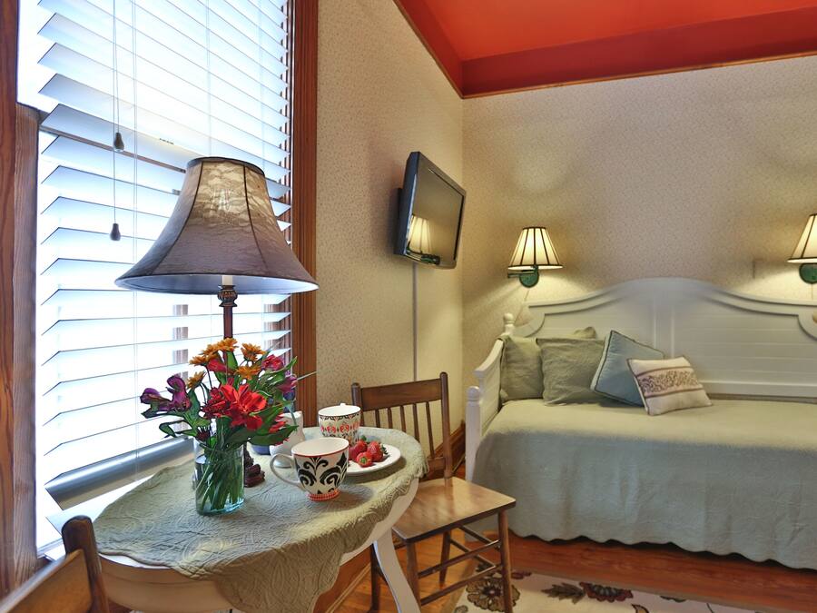 A bedroom with a bed, bedside lamps, a bedside table with a lamp, a chair, and a window with blinds.