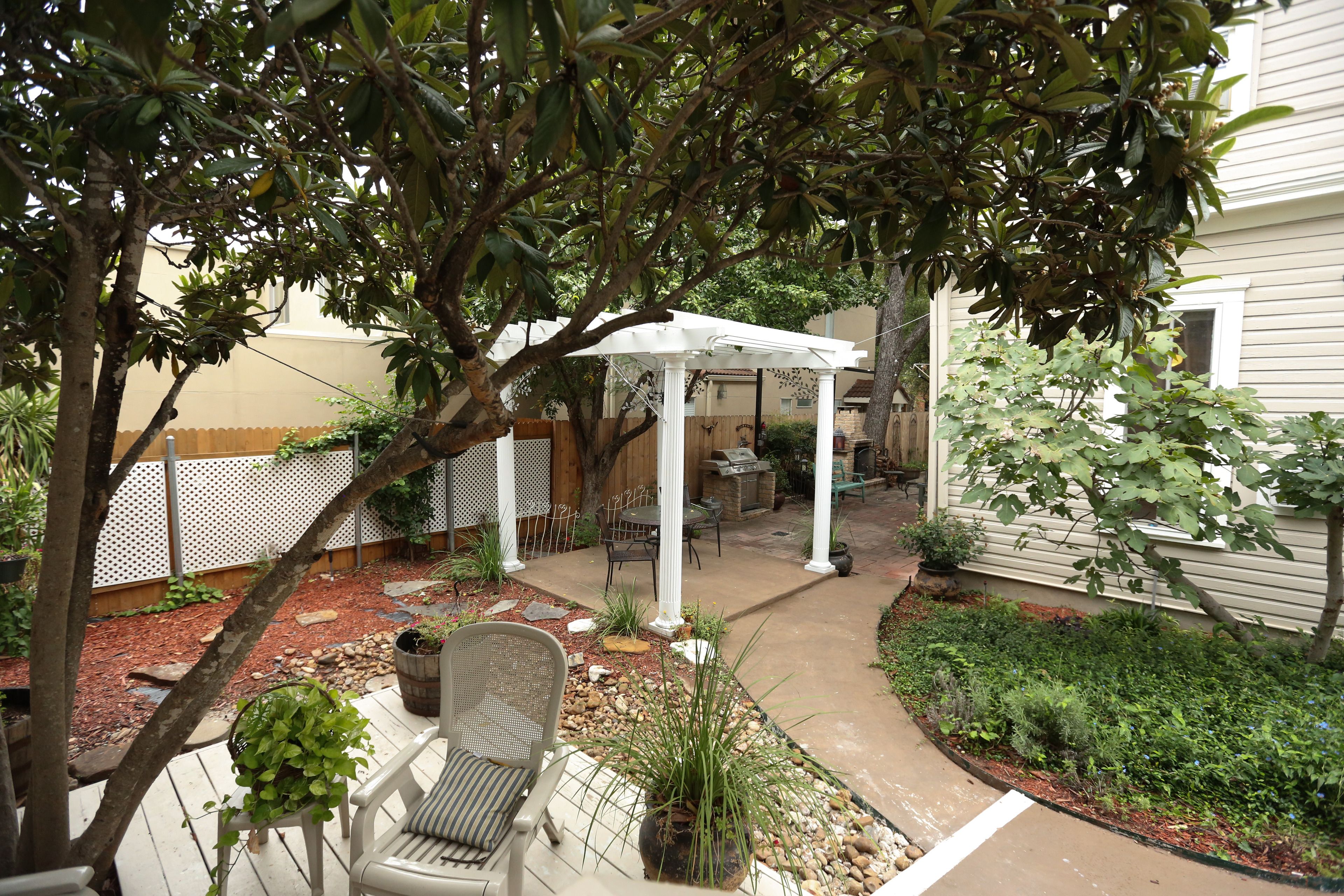 Eine Terrasse mit weißem Pergola, Gartenmöbeln und einem Blumenbeet mit verschiedenen Pflanzen.
