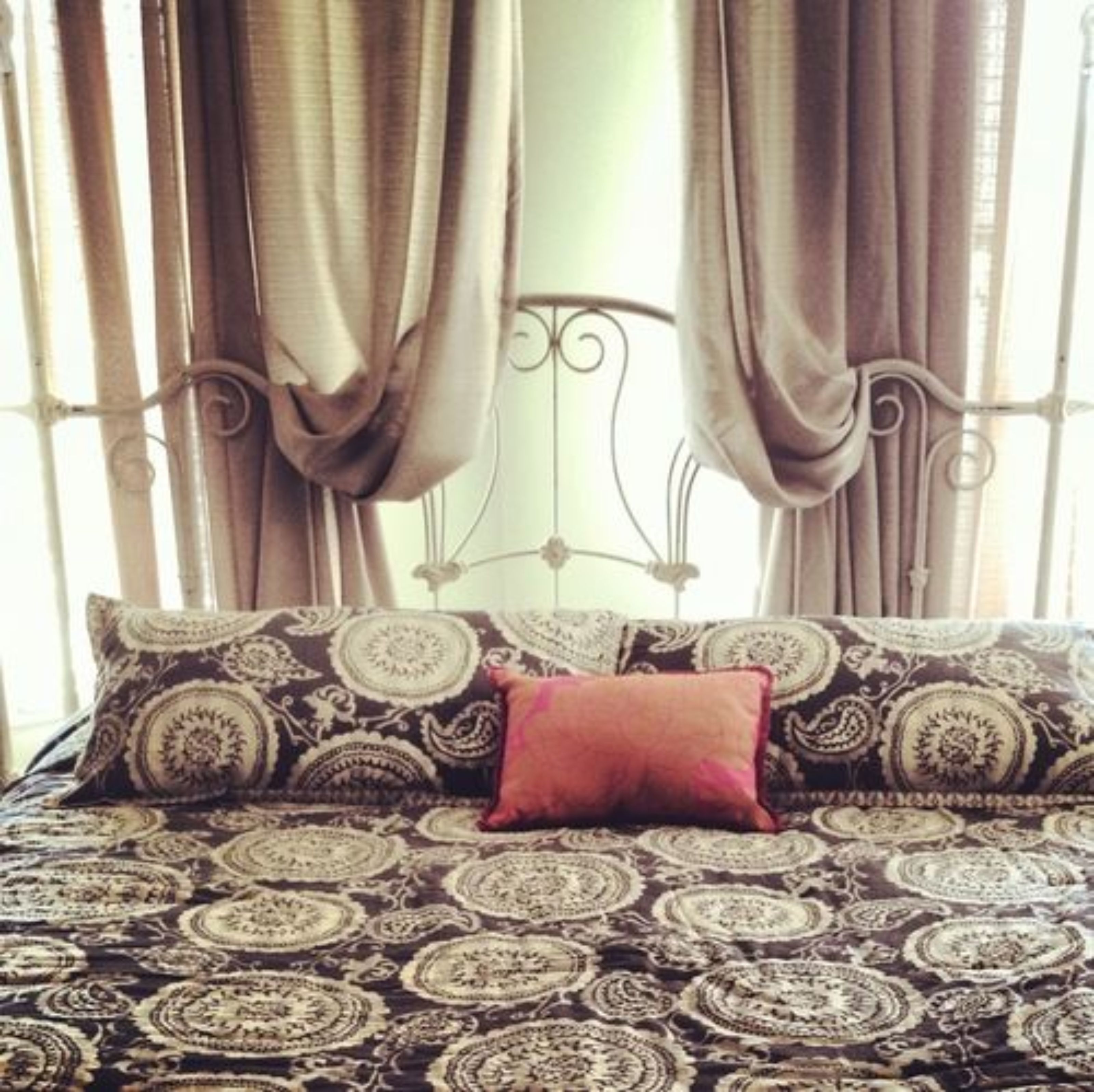 Una cama con una colcha estampada y una almohada roja.