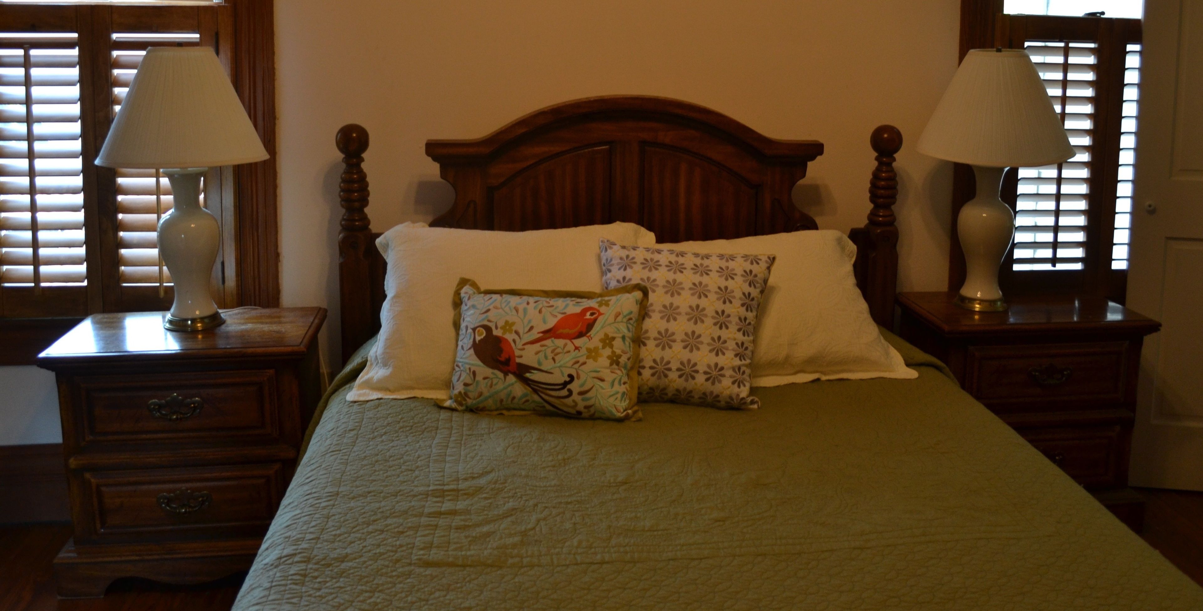 A neatly made bed with a green bedspread, two pillows, and two bedside lamps on wooden nightstands.