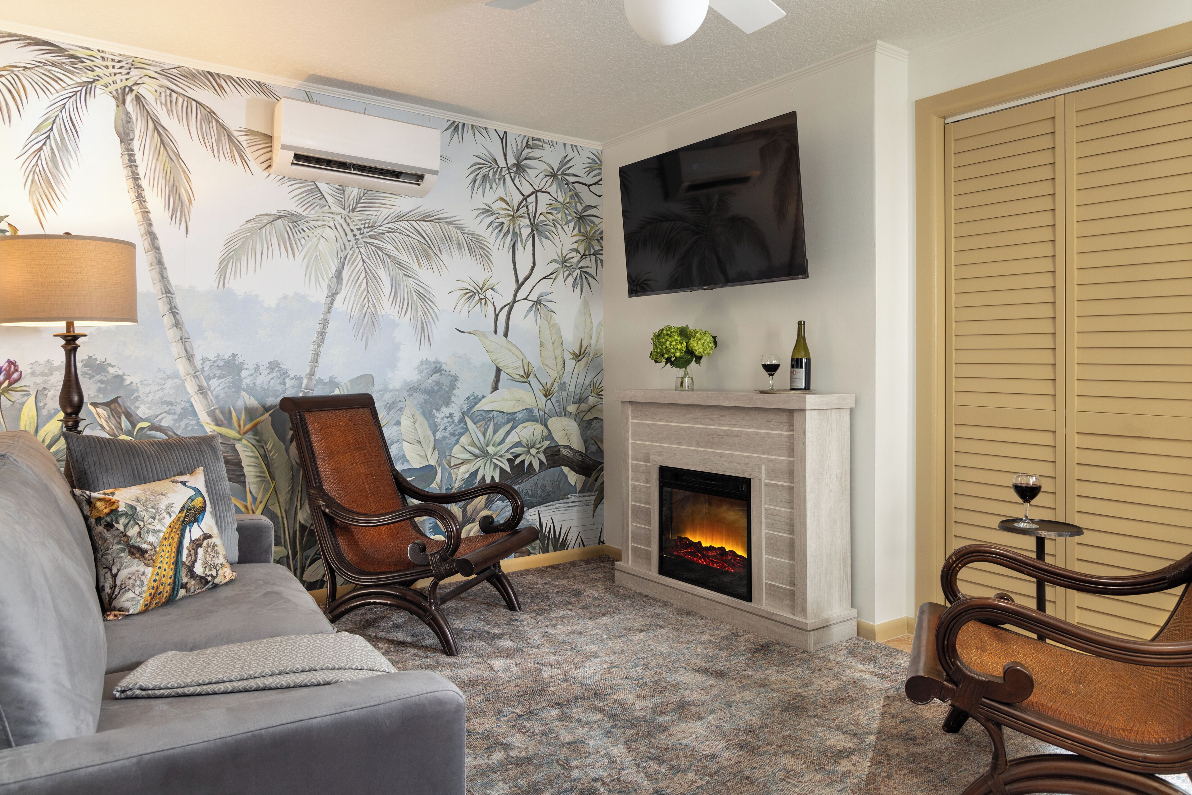 Una sala de estar con chimenea, un sofá, un sillón y un televisor montado en la pared.