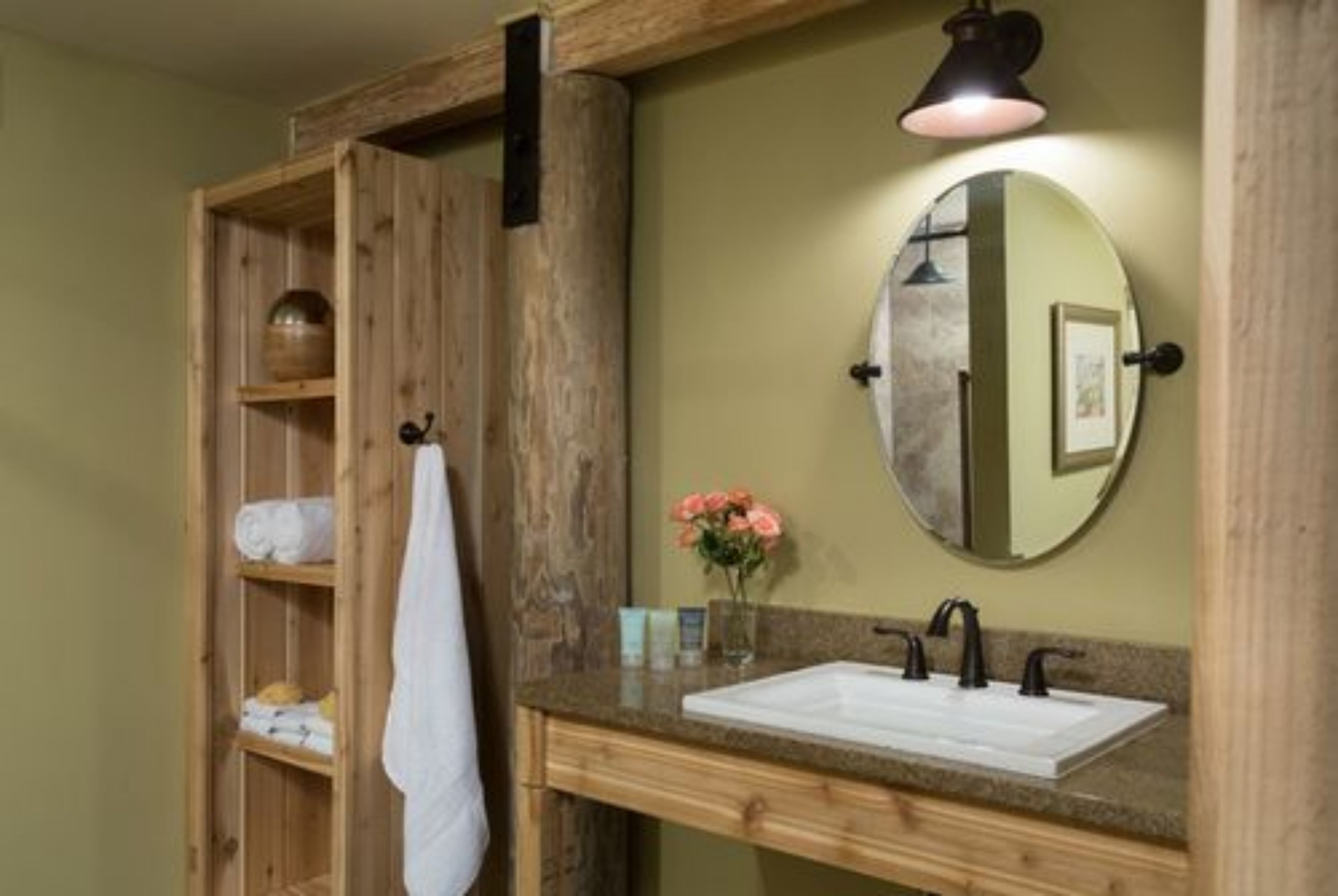 A bathroom with a wooden vanity, a round mirror, and a towel rack.