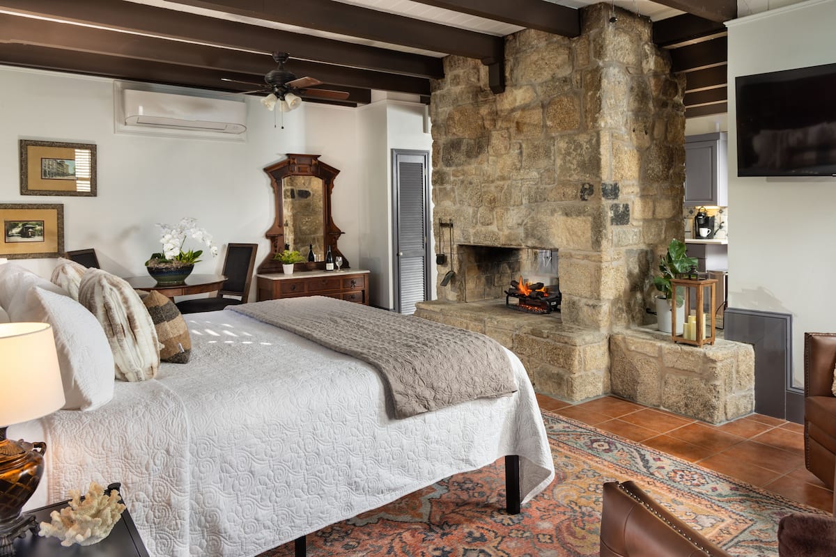 A bedroom with a stone fireplace, a bed with a white quilt, and a large mirror.