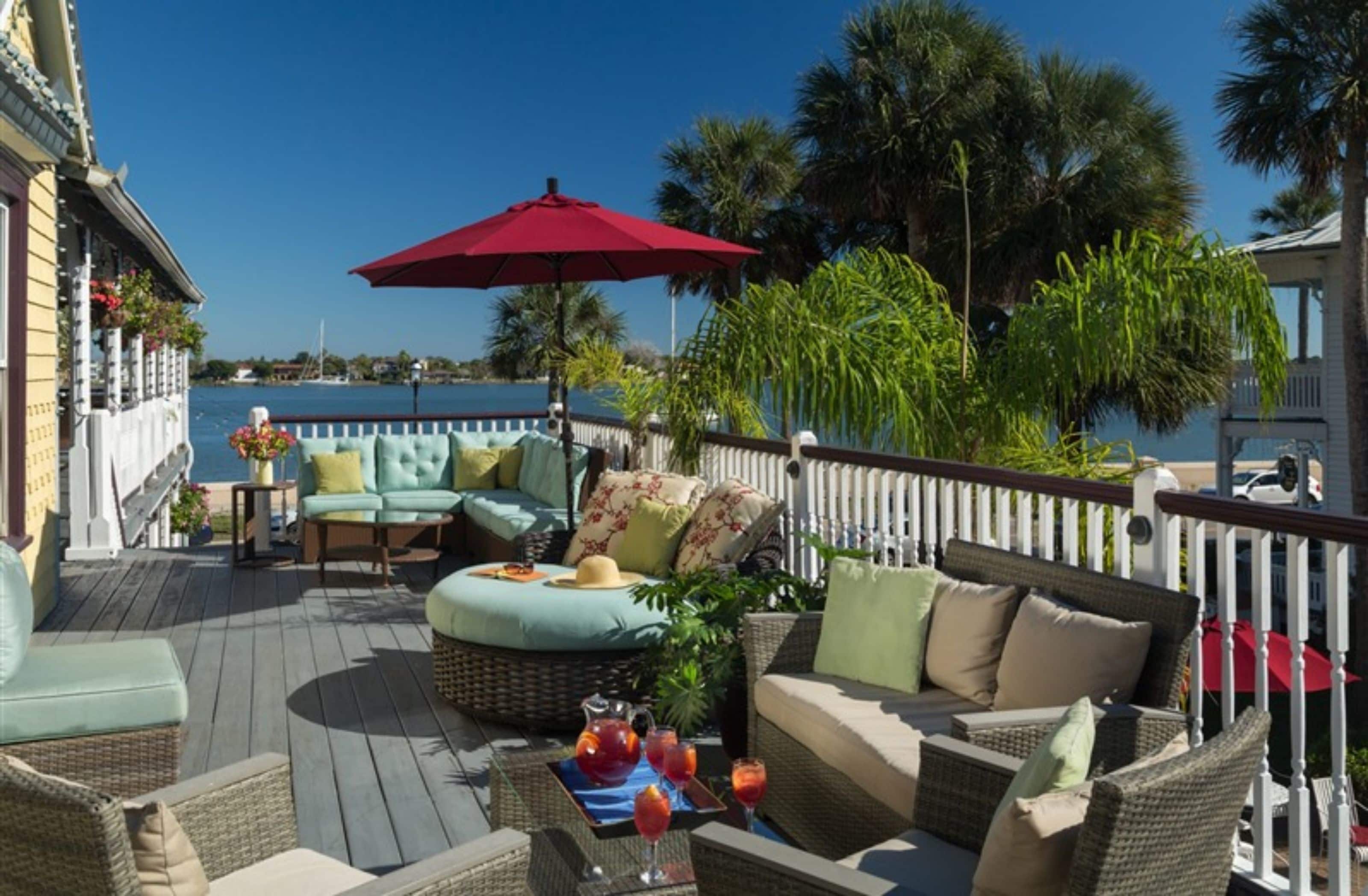 A deck with wicker furniture, a red umbrella, and a view of the water.