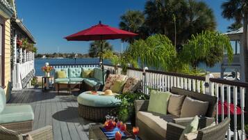 A deck with wicker furniture, a red umbrella, and a view of the water.