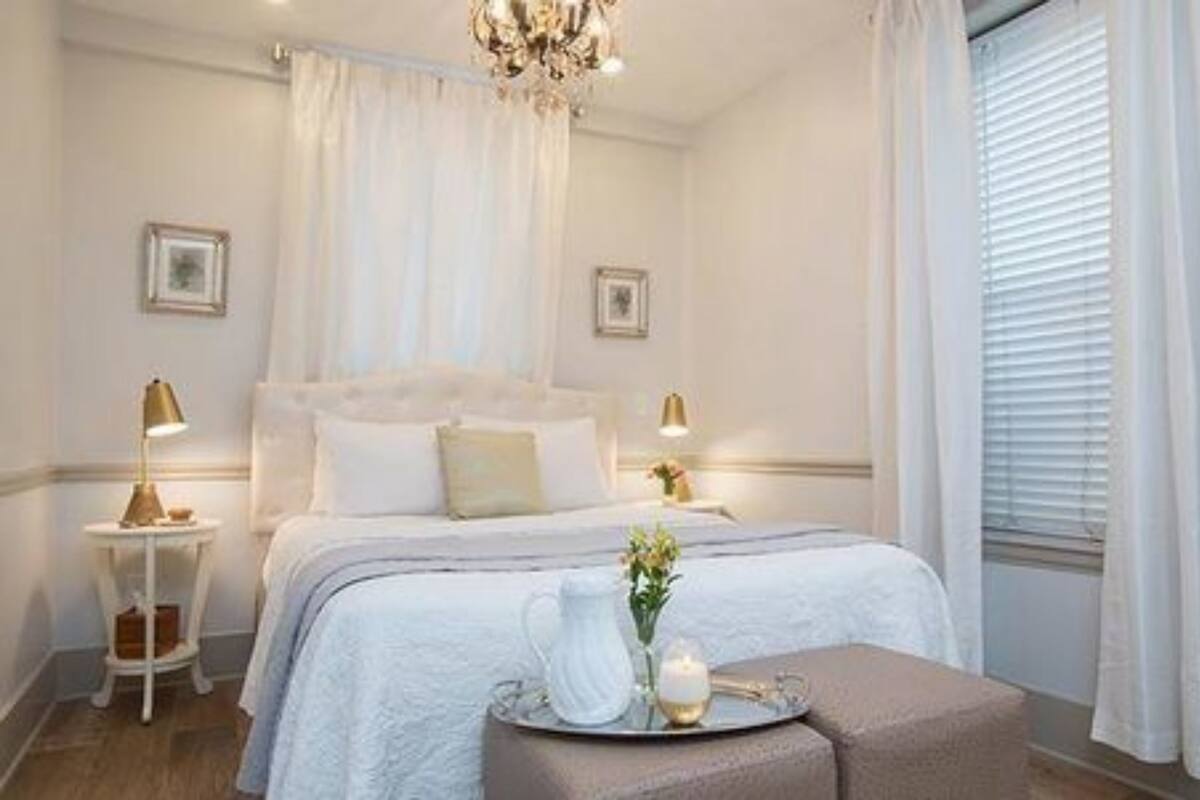 A bedroom with a large bed, bedside lamps, a chandelier, and a window with blinds.
